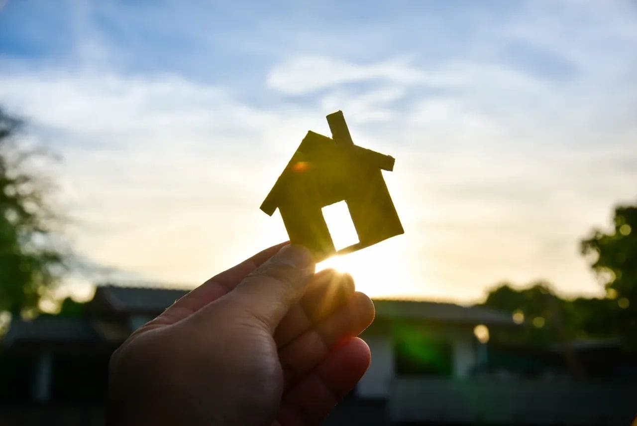 A person holding up a small house in front of the sun.