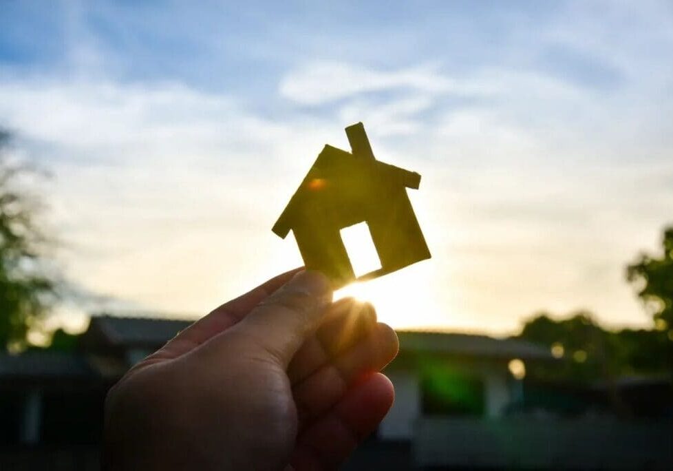 A person holding up a small house in front of the sun.